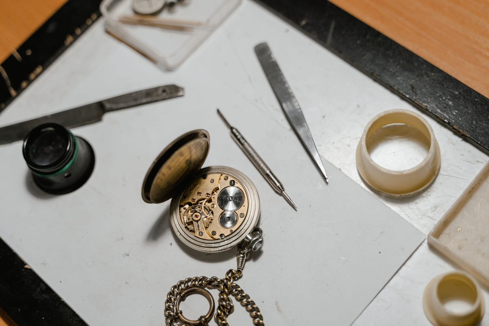 Watchmaker's tools laid beside an opened pocket watch on a bench